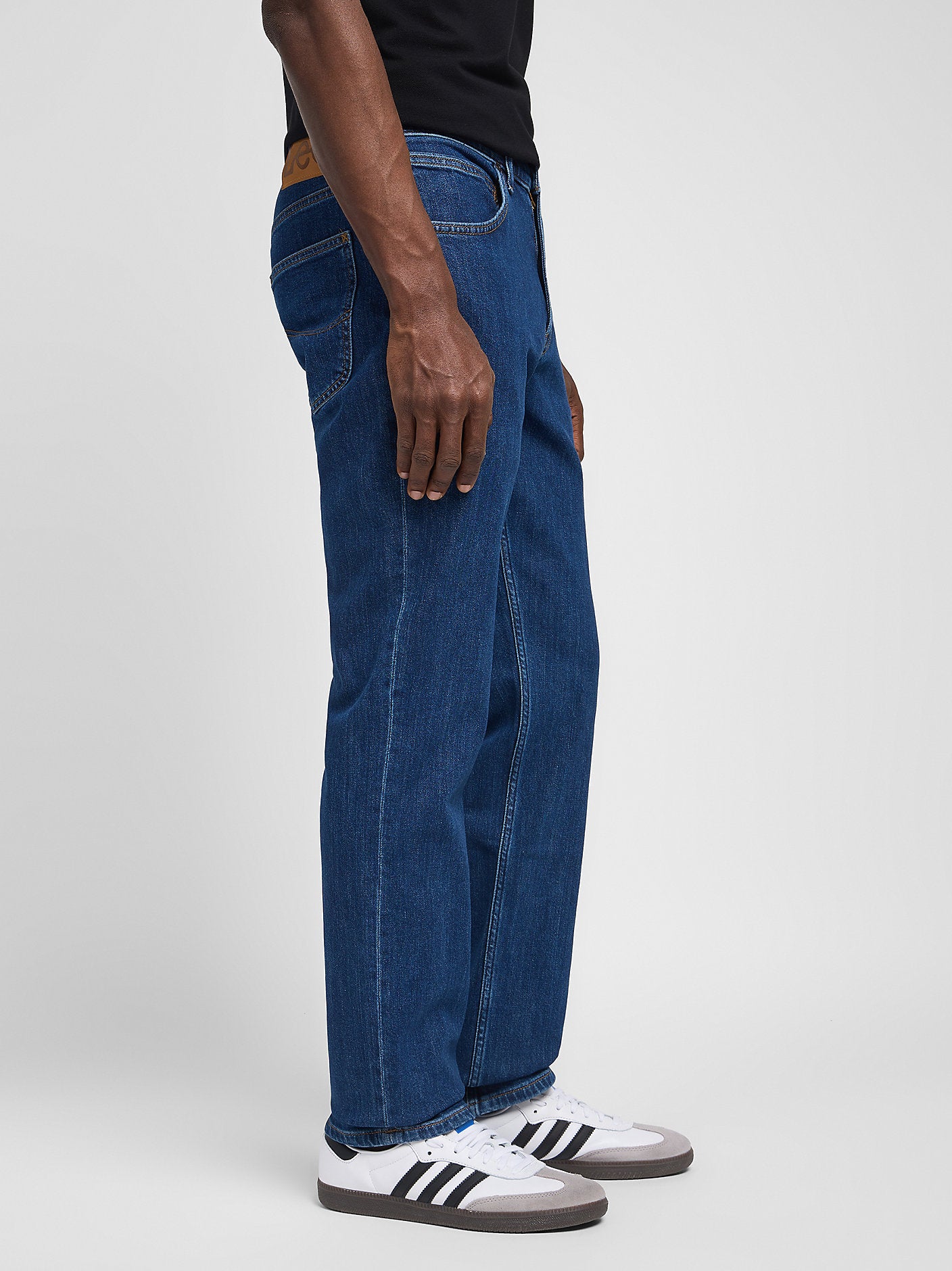 Person wearing blue jeans and white sneakers with black stripes on a light gray background