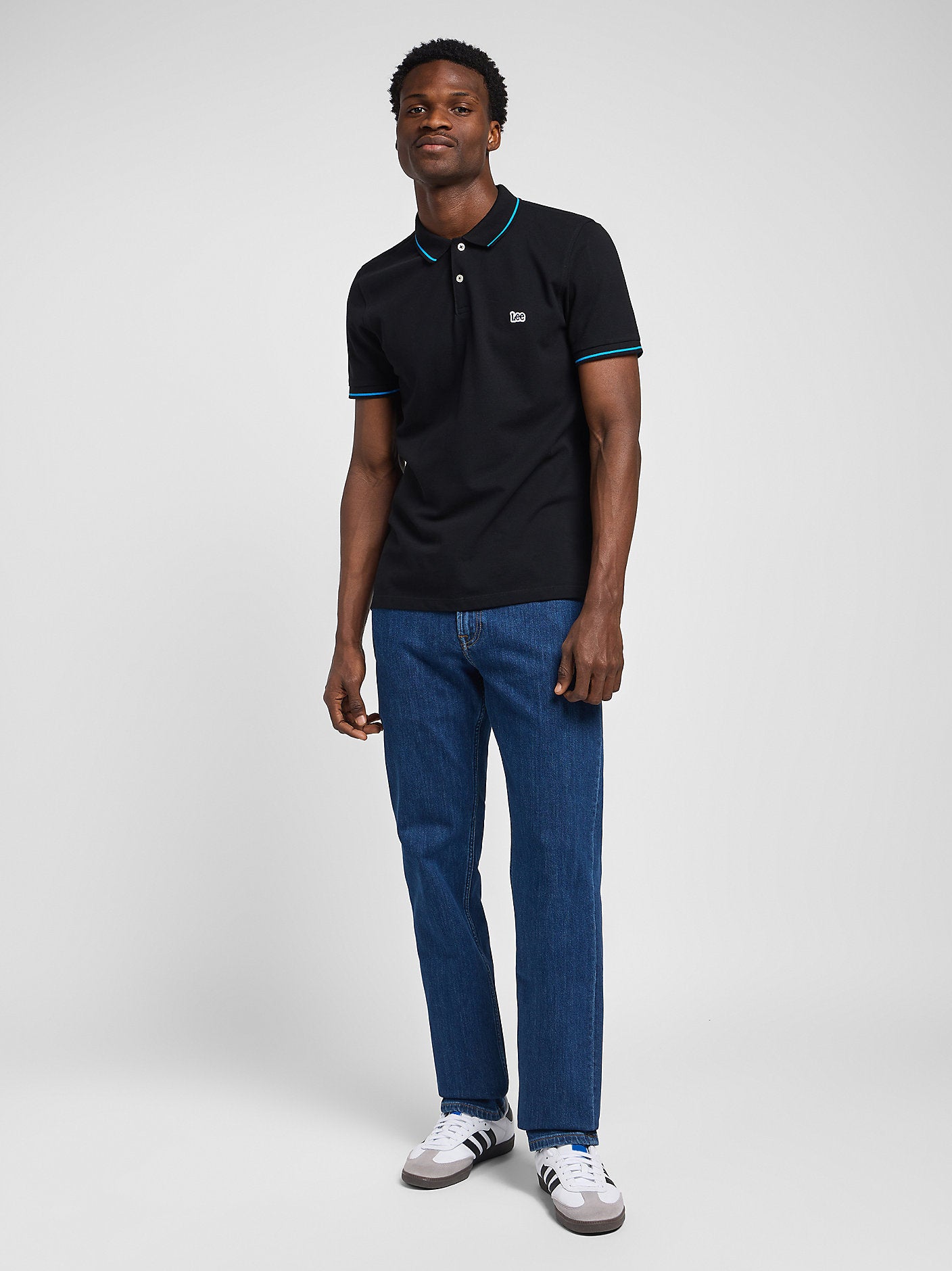 Man wearing a black polo shirt and blue jeans on a white background