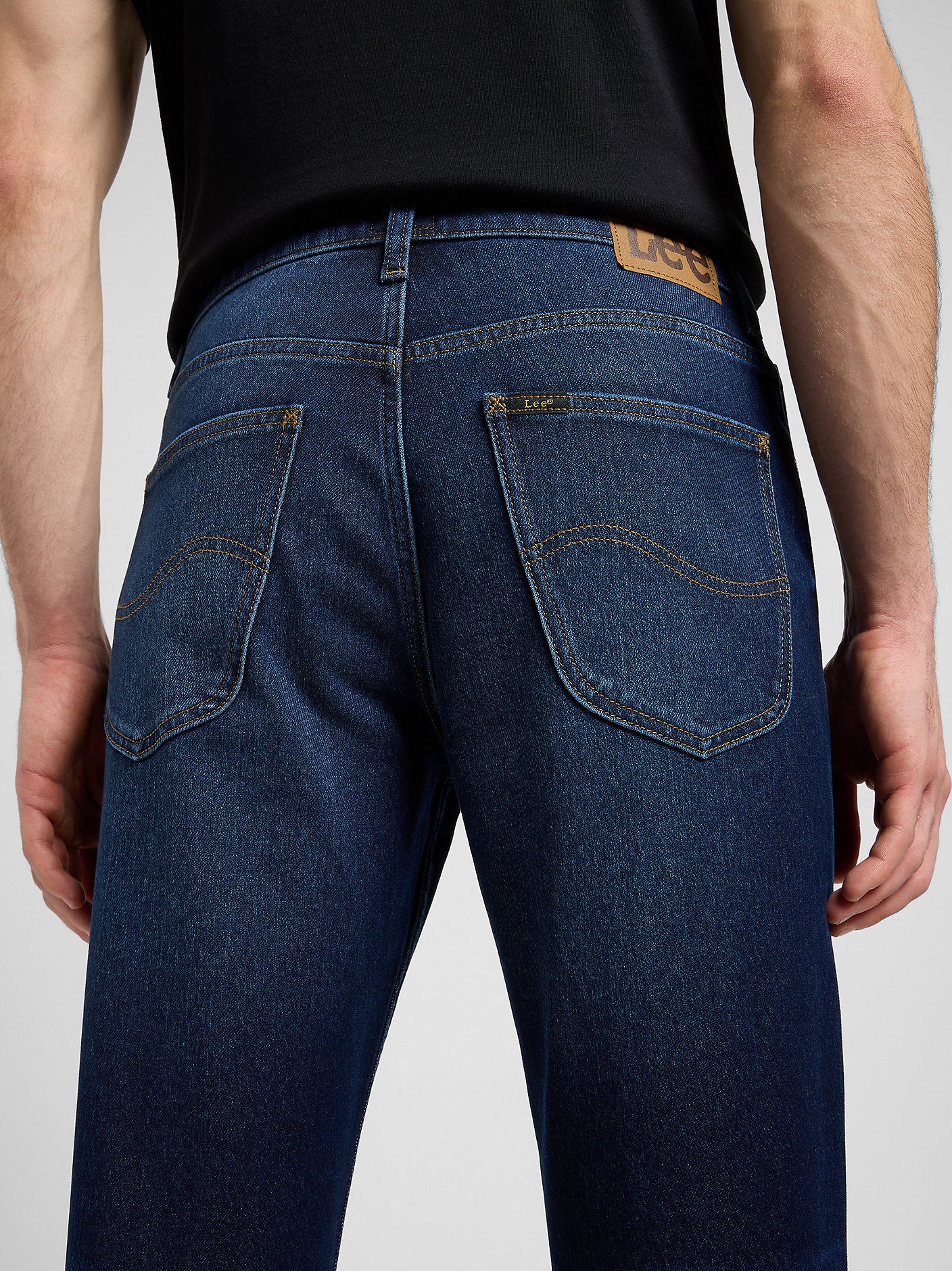 Person wearing blue jeans with a visible brand logo on a plain background