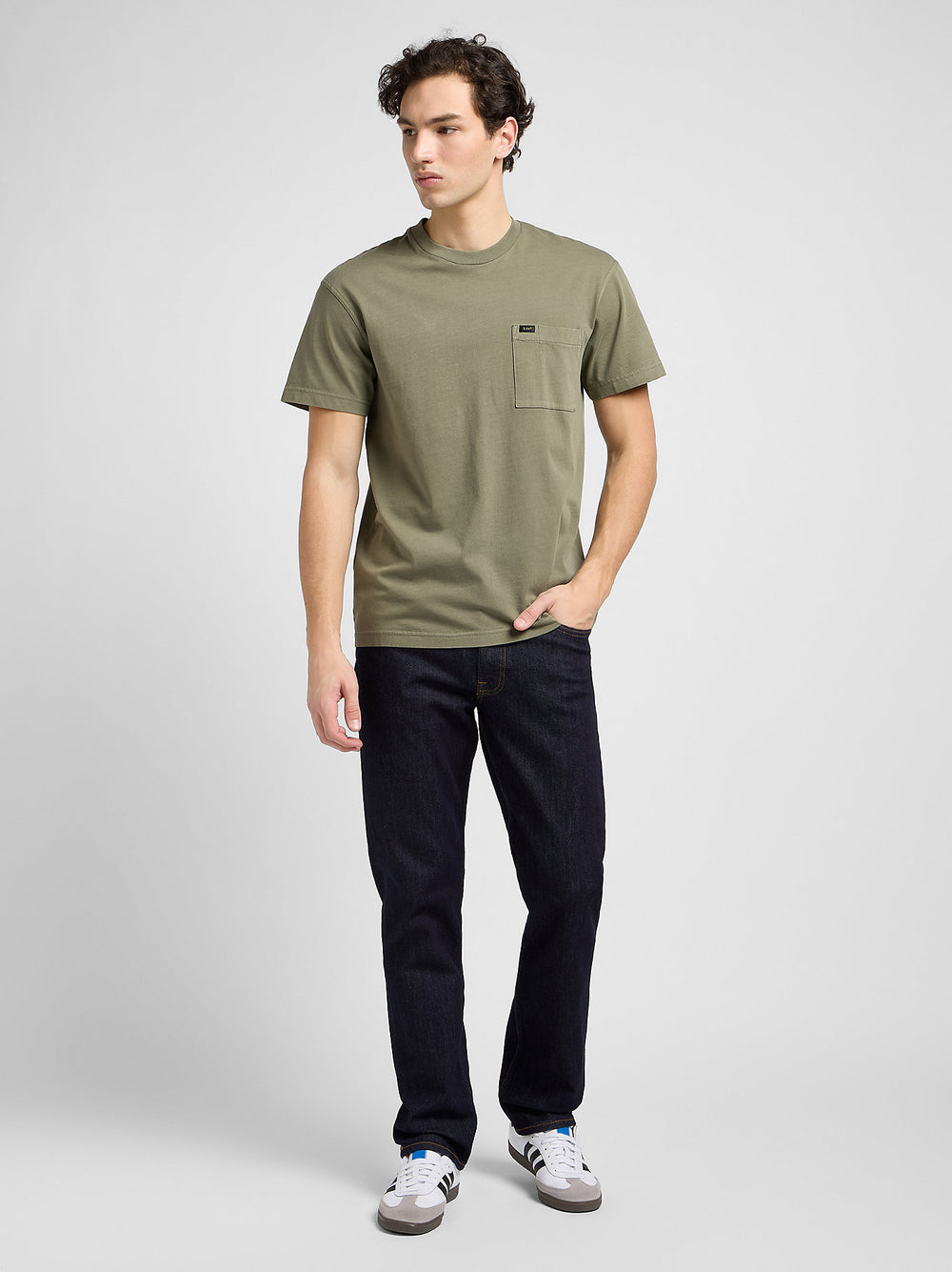 Man wearing an olive green t-shirt and black jeans on a white background