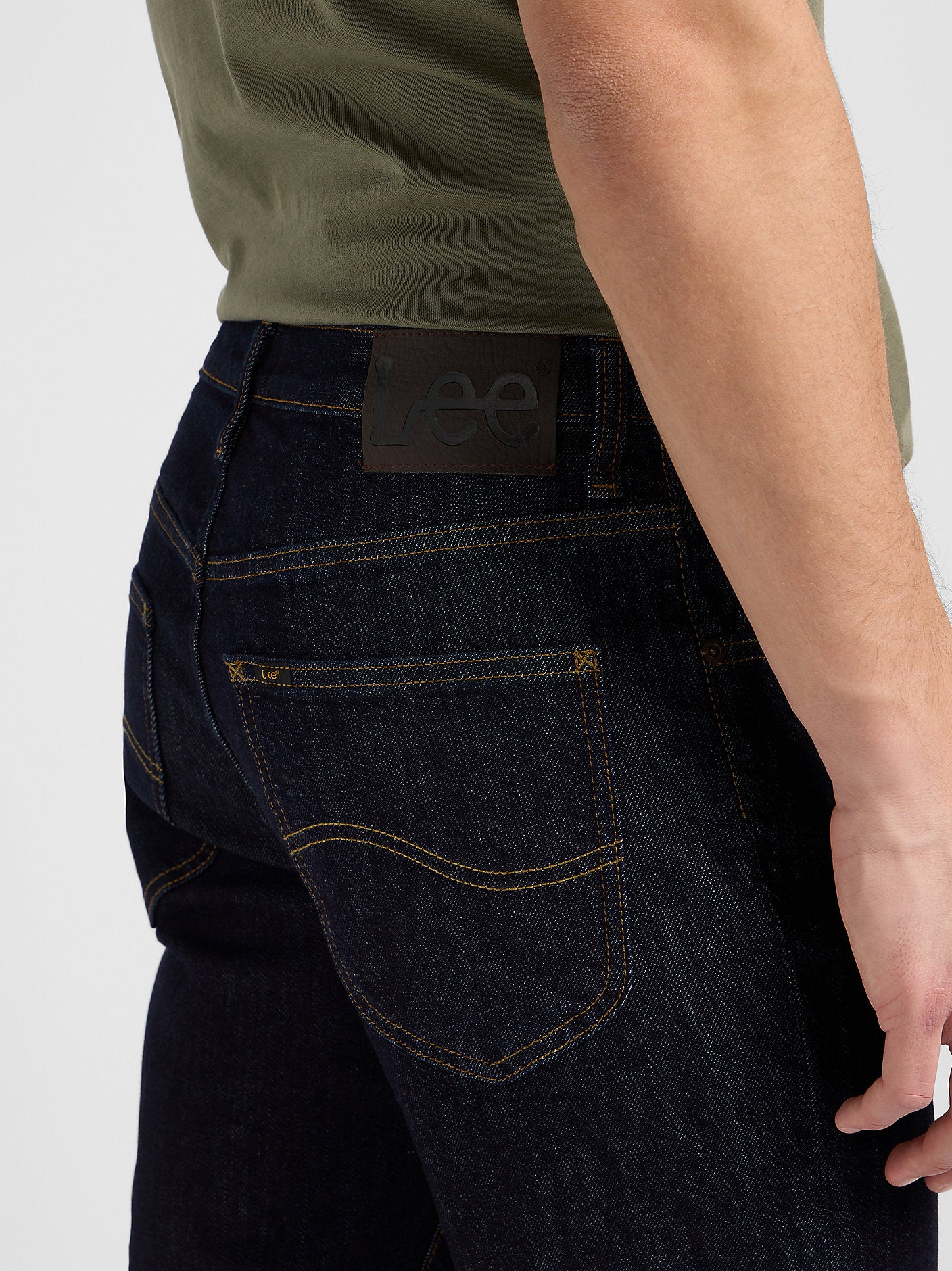 Person wearing dark blue jeans with a visible Lee brand label on a white background