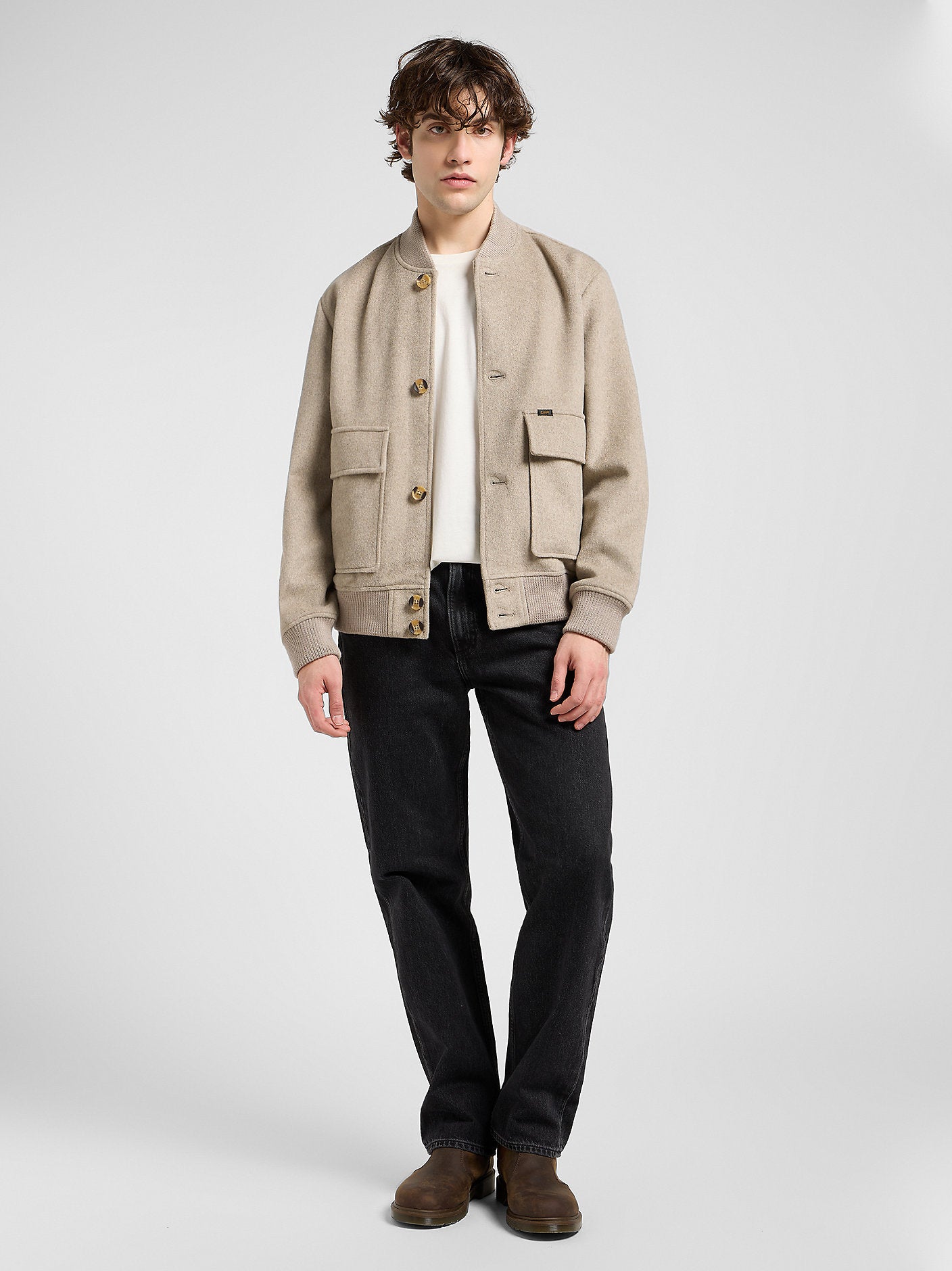 Man wearing a beige jacket, white shirt, black pants, and brown shoes on a white background