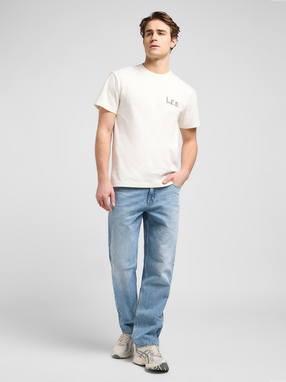 Man wearing a white t-shirt and light blue jeans on a gray background
