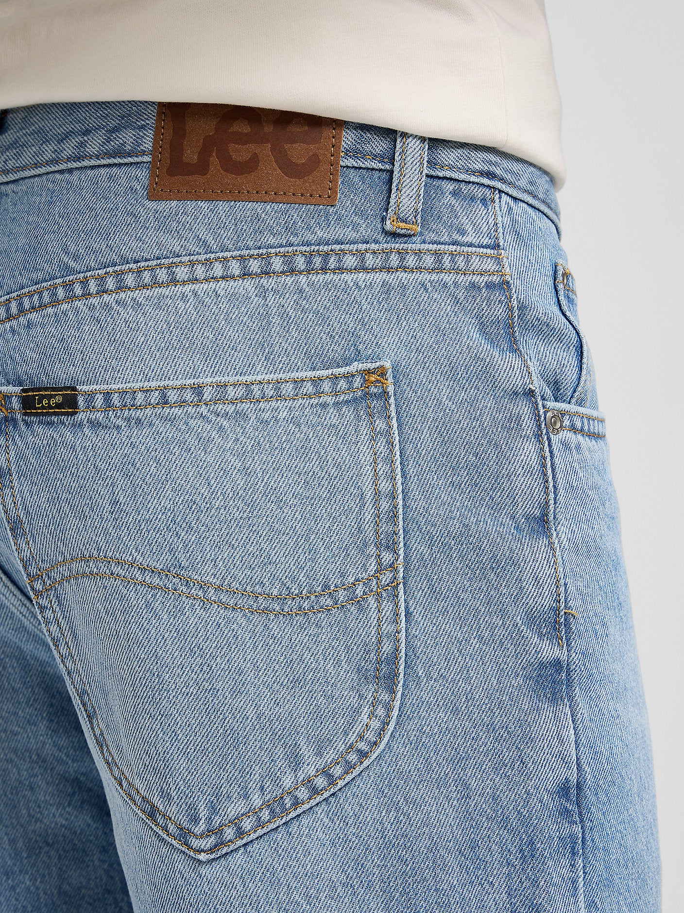 Close-up of blue jeans with a visible Lee brand label on a white background