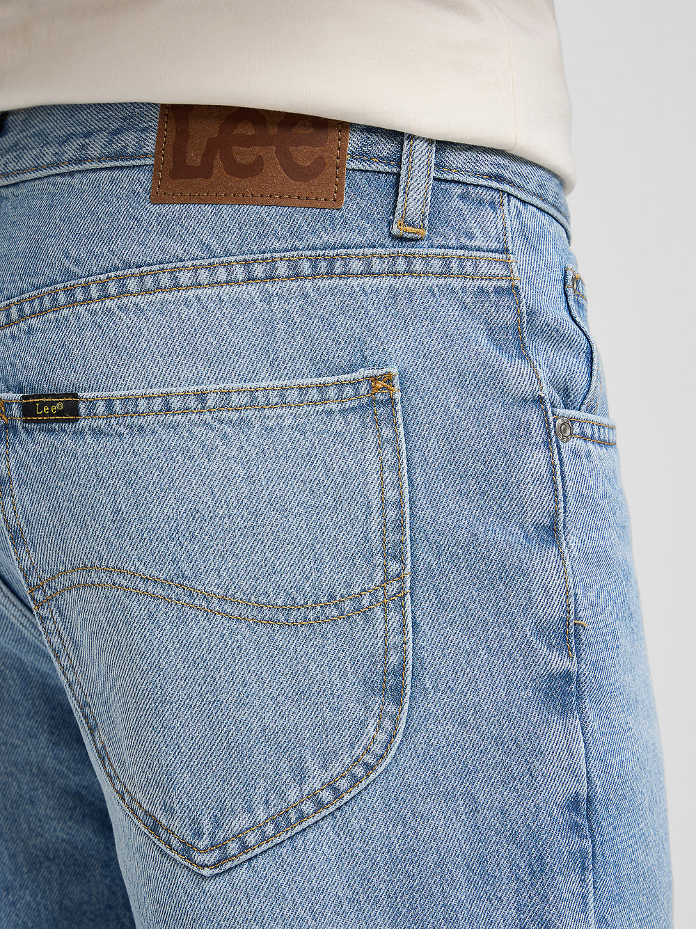 Close-up of blue jeans with a visible Lee brand label on a white background