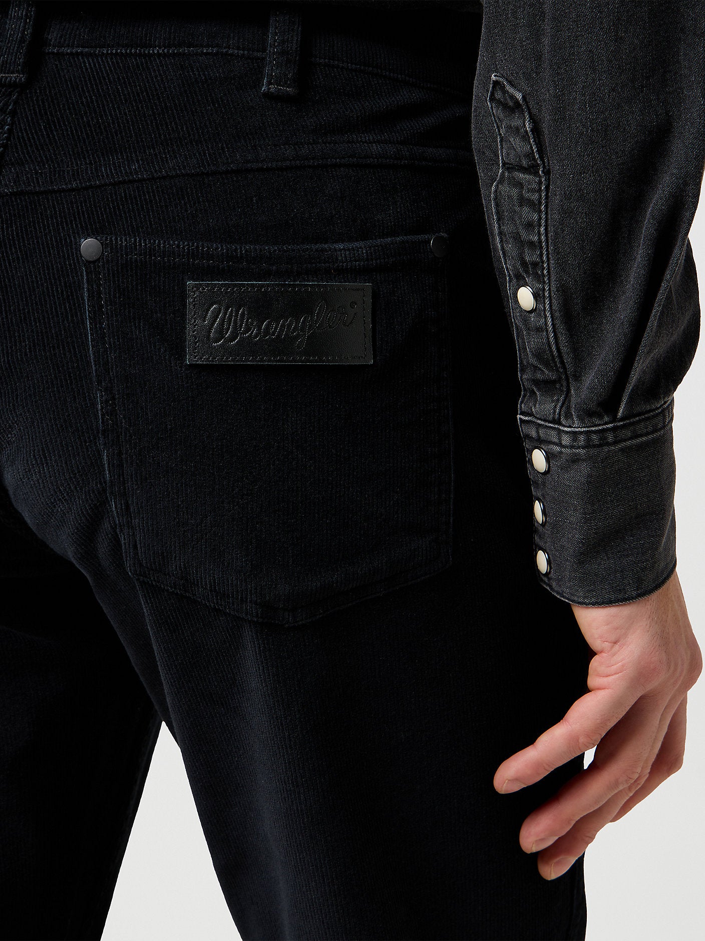 Close-up of black denim jeans with a brand label on a white background