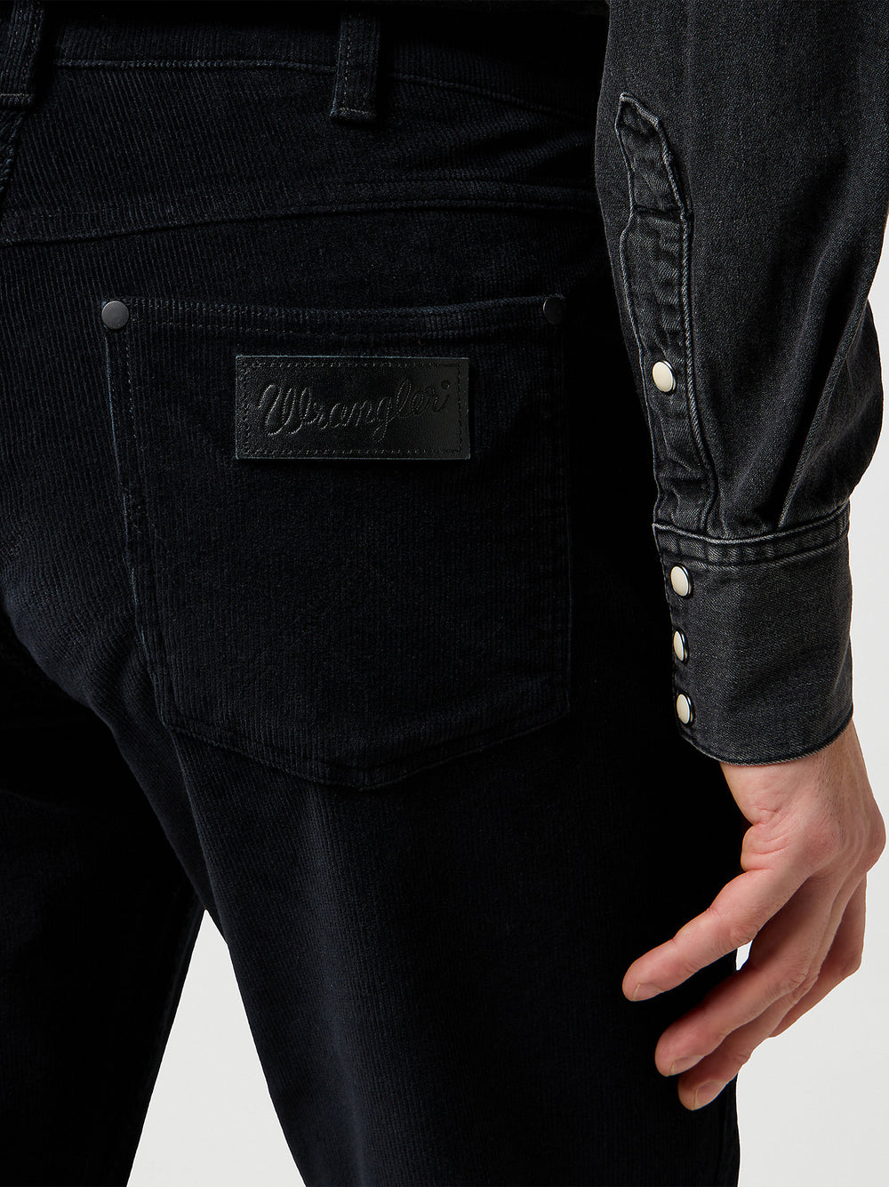 Close-up of black denim jeans with a brand label on a white background