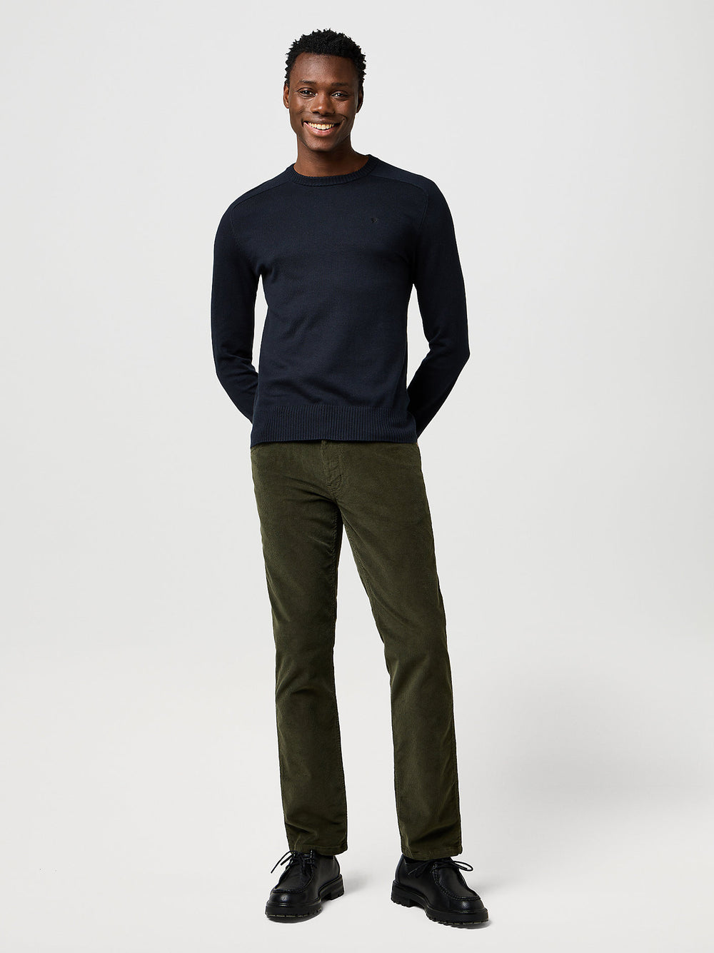 Man wearing a navy sweater and green pants on a white background