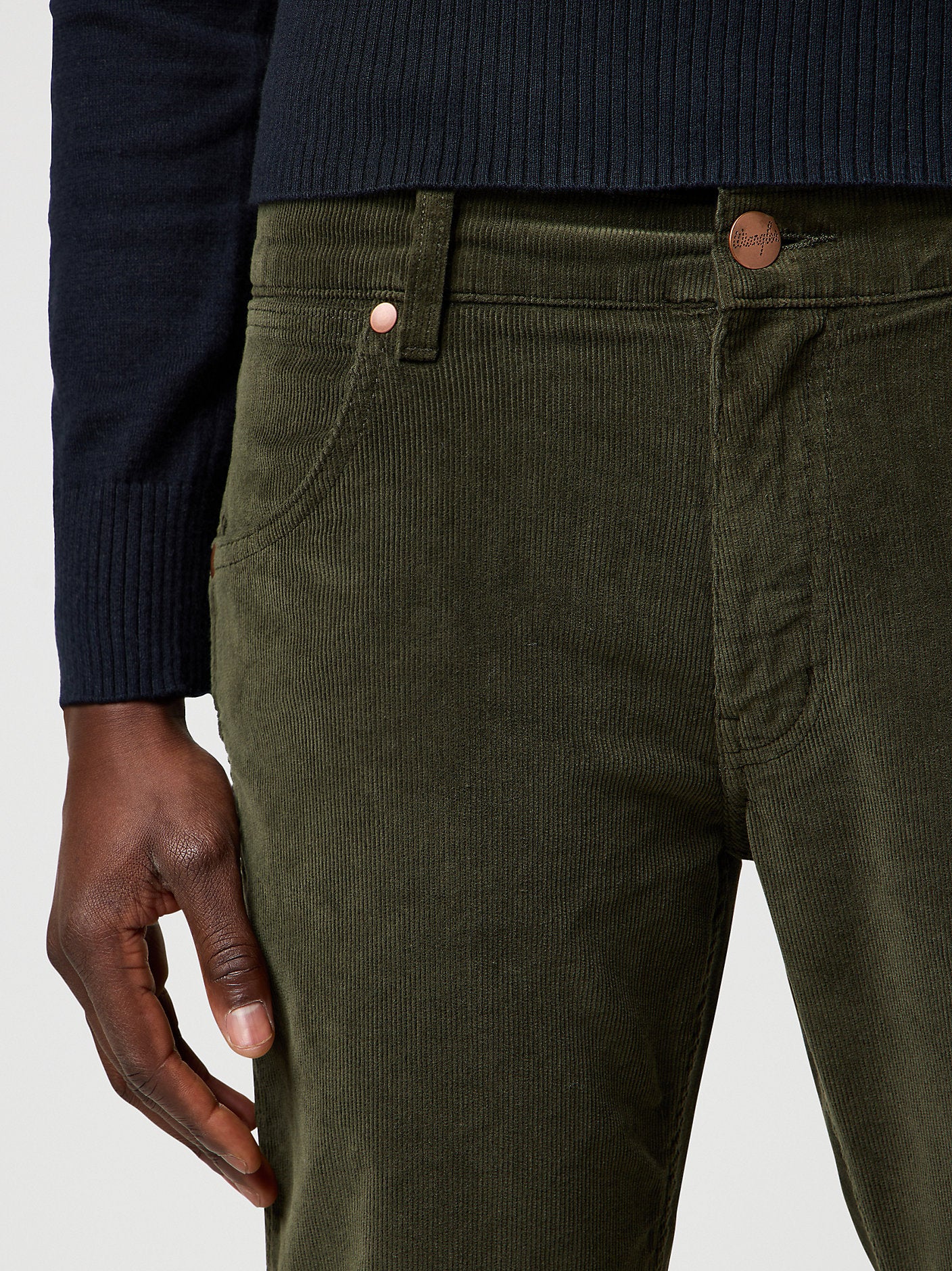Close-up of green corduroy pants with a navy sweater and hand visible.
