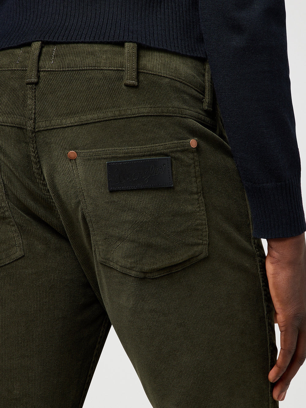Close-up of olive green pants with a patch on the back pocket against a white background