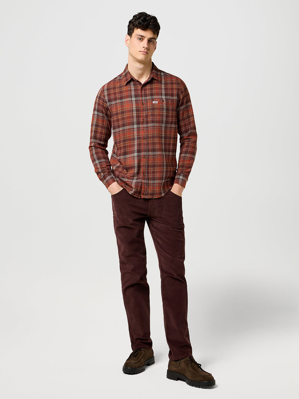 Man wearing a plaid shirt and brown pants on a white background