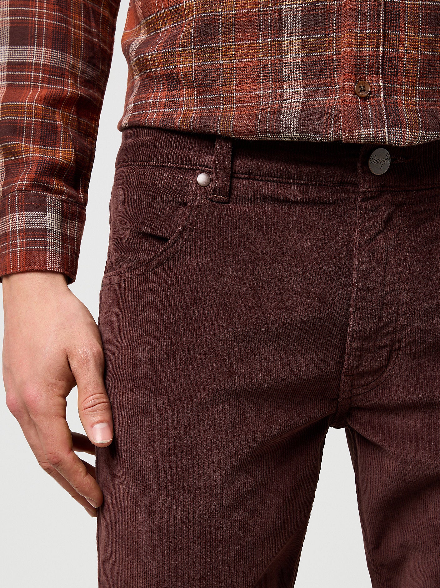Brown corduroy pants worn with a plaid shirt on a light gray background