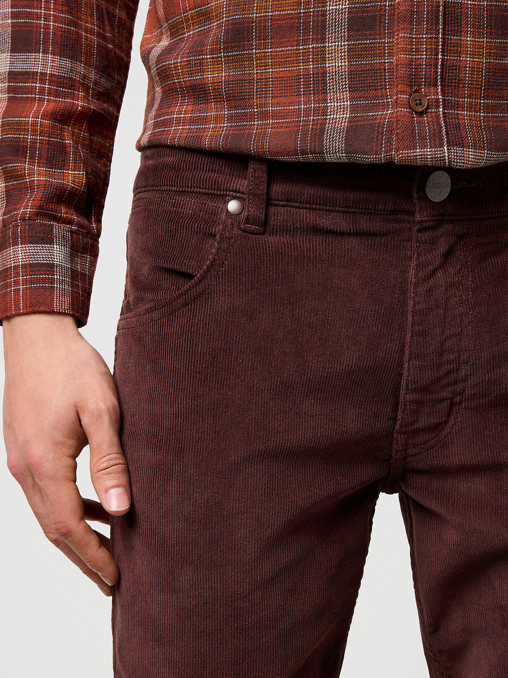 Brown corduroy pants worn with a plaid shirt on a light gray background