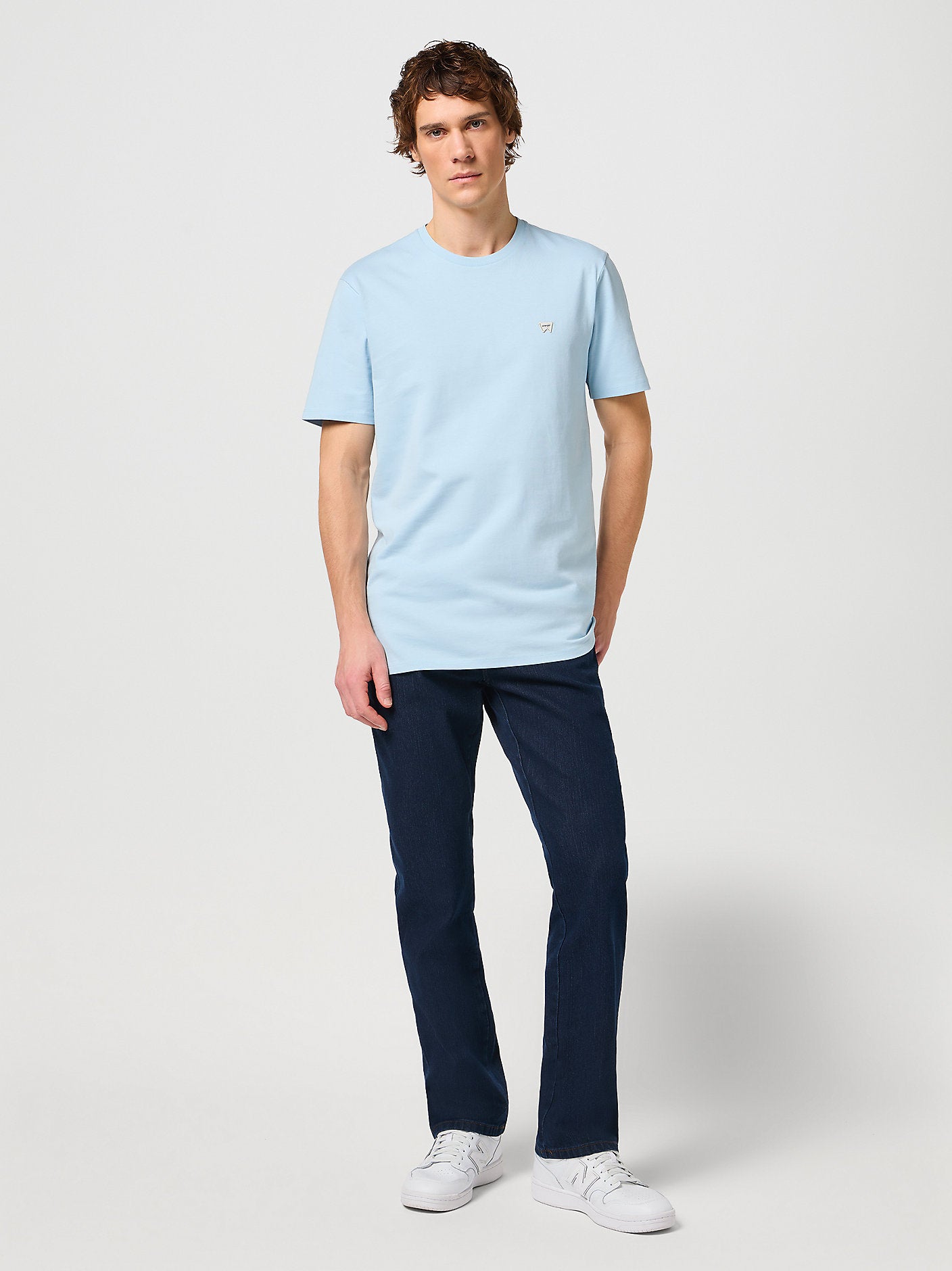 Man wearing a light blue t-shirt and dark blue pants on a white background