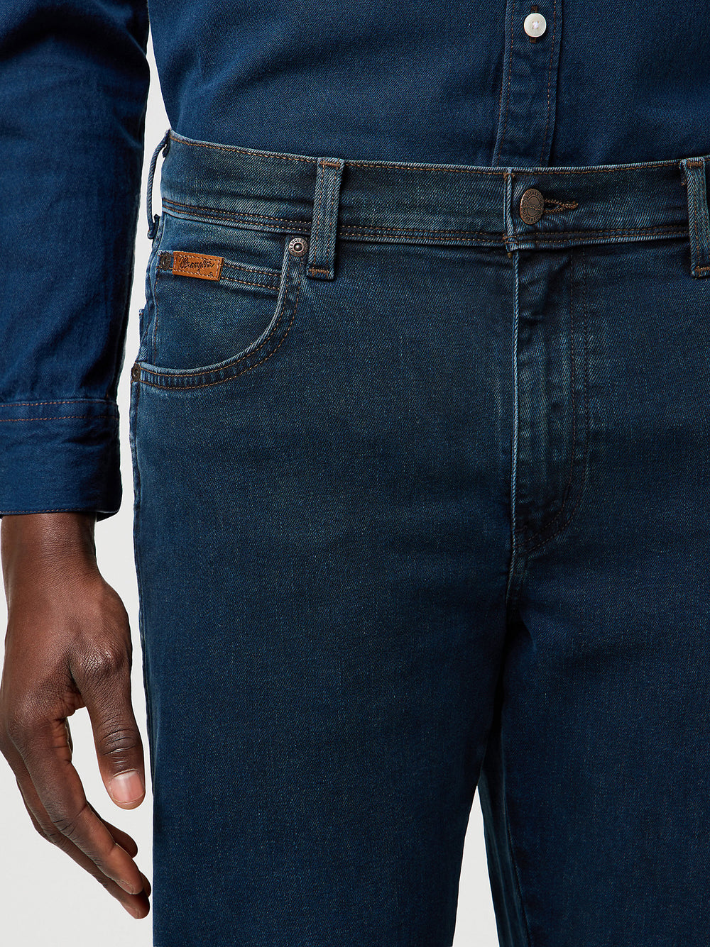 Close-up of dark blue jeans with a brand label on a light gray background