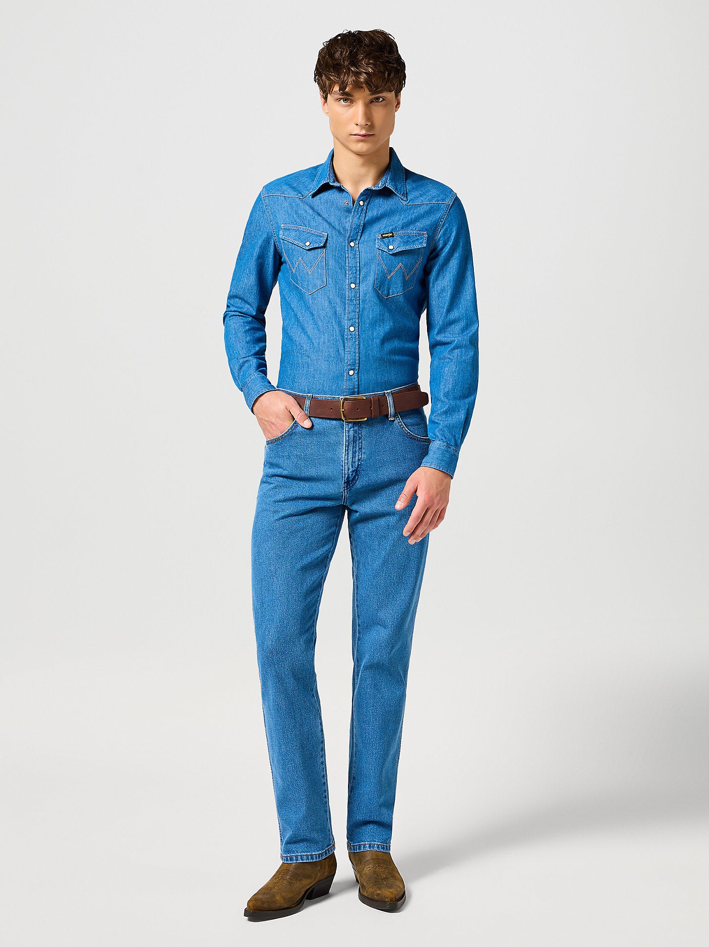 Man wearing a blue denim shirt and jeans on a white background